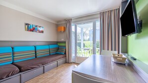 A modern kitchen with a wooden countertop, a built-in bench with colorful cushions, a flat-screen TV mounted on the wall, and a sliding glass door leading to an outdoor area. - Danou - Appartement avec Terrasse (Courseulles-sur-Mer)