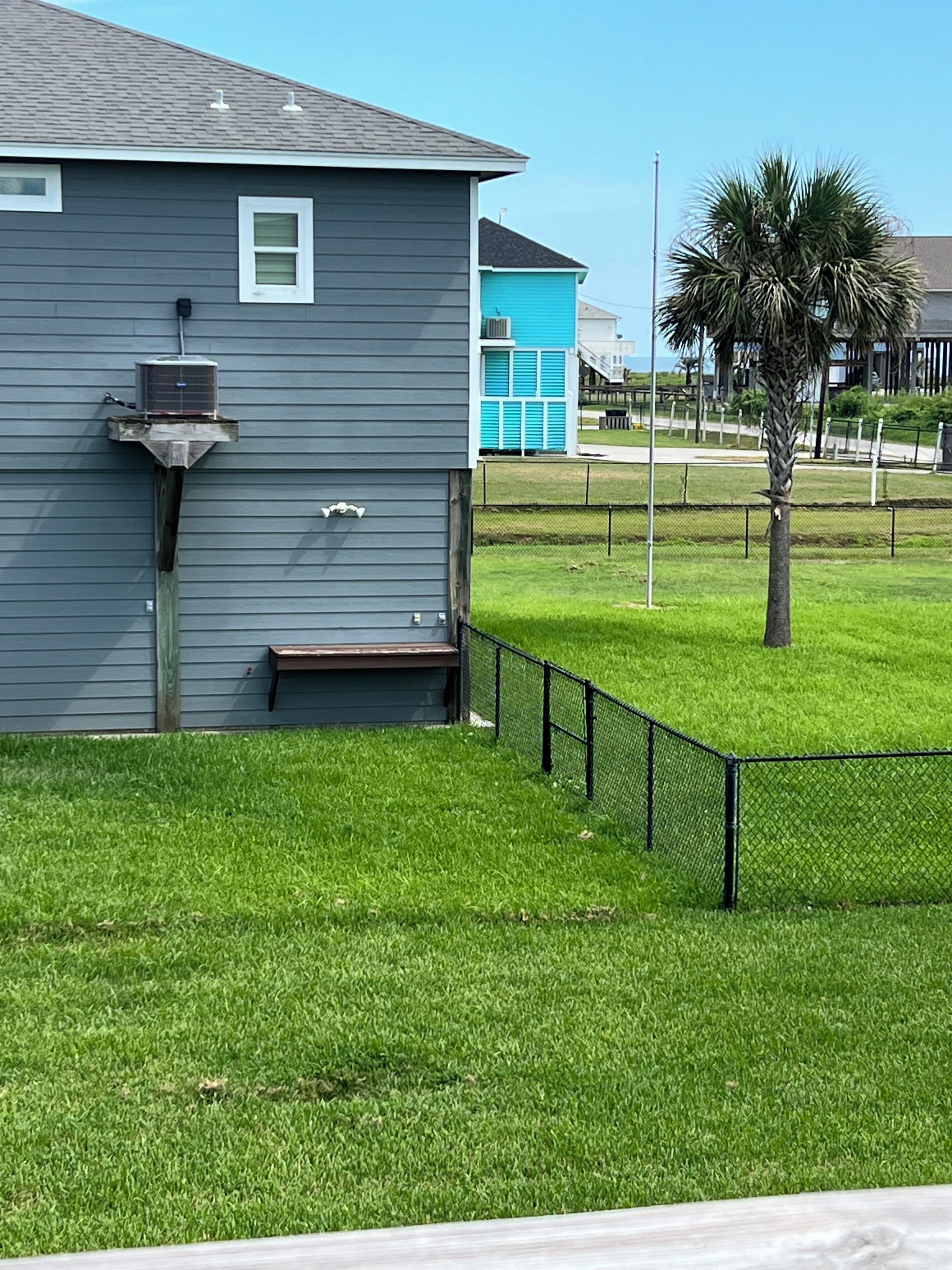 A residential building with a grey exterior, a small porch, and a fenced yard with a palm tree.