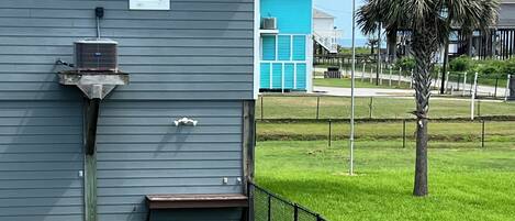 A residential building with a grey exterior, a small porch, and a fenced yard with a palm tree.