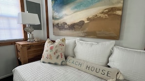 Un dormitorio con cama, un cuadro de una playa, una lámpara y un aparador.