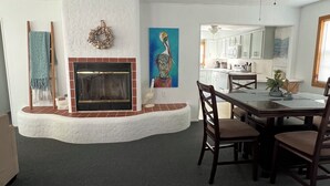 Una sala de estar con chimenea, comedor y cocina al fondo.