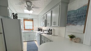 Una cocina con encimera blanca, ventilador de techo y ventana con persianas.