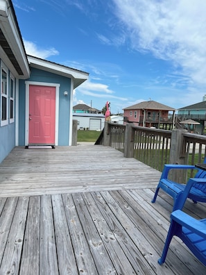 A wooden deck with a pink door, a blue chair, and a pink flamingo statue.