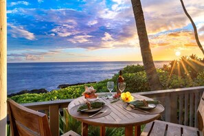 Romantic round-table lanai setup under palm trees at golden hour. - Oceanfront Luxury 4BR Beach House w/ AC, Lanai, Sunset Views & Walk to the Beach (Kailua Kona)