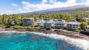 Un hotel frente al mar con aguas turquesas cristalinas, una costa rocosa y edificios de varios pisos con grandes ventanales.