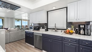 Una cocina moderna con armarios oscuros, una encimera blanca y un área de comedor con un sofá gris.
