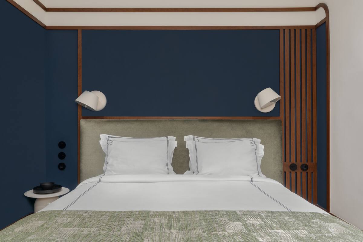 Un letto rifatto con lenzuola bianche e una coperta a motivi verdi. Due abat-jour su ciascun lato del letto.