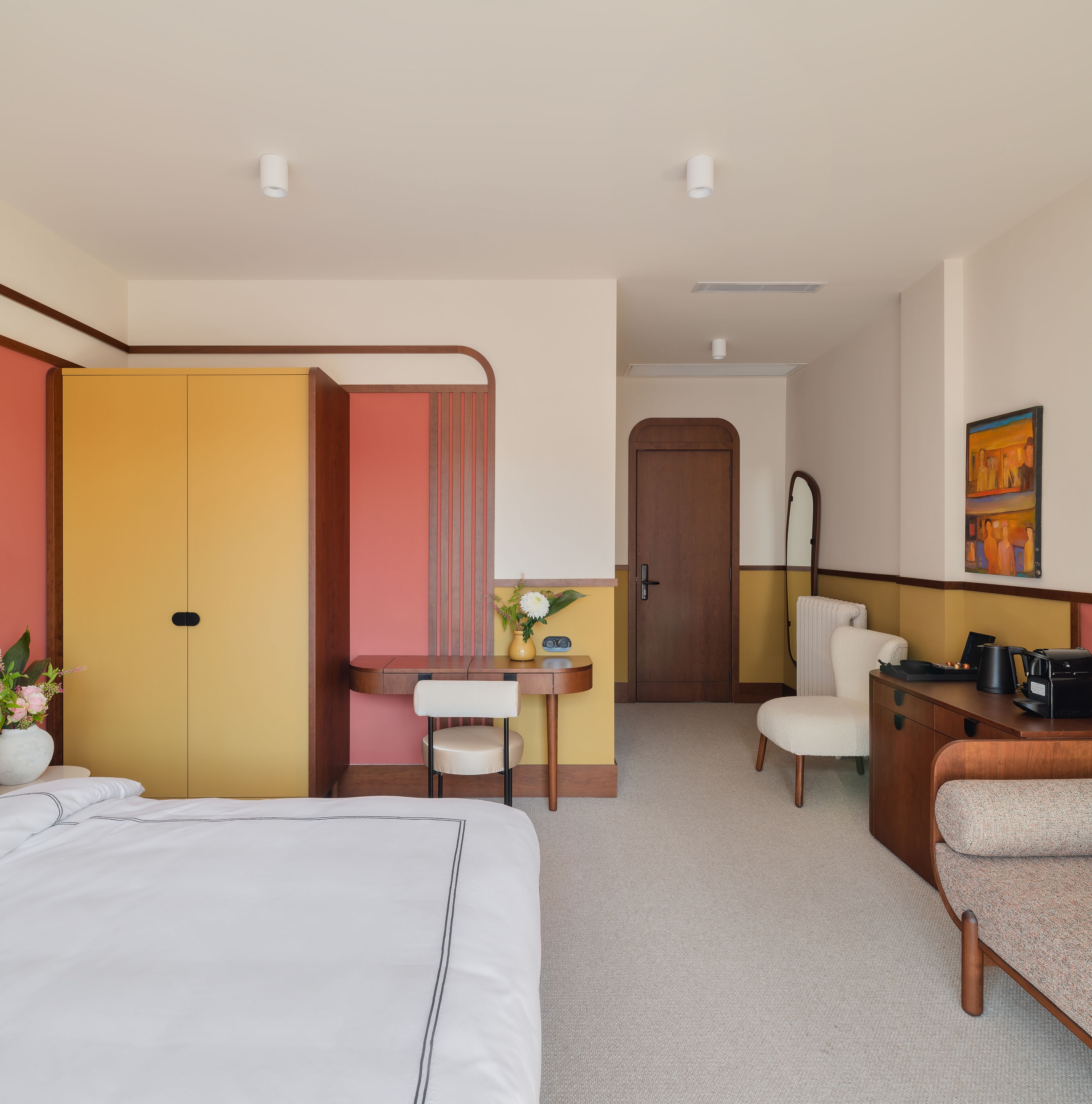 A hotel room with a bed, a desk, a chair, a wardrobe, and a door.