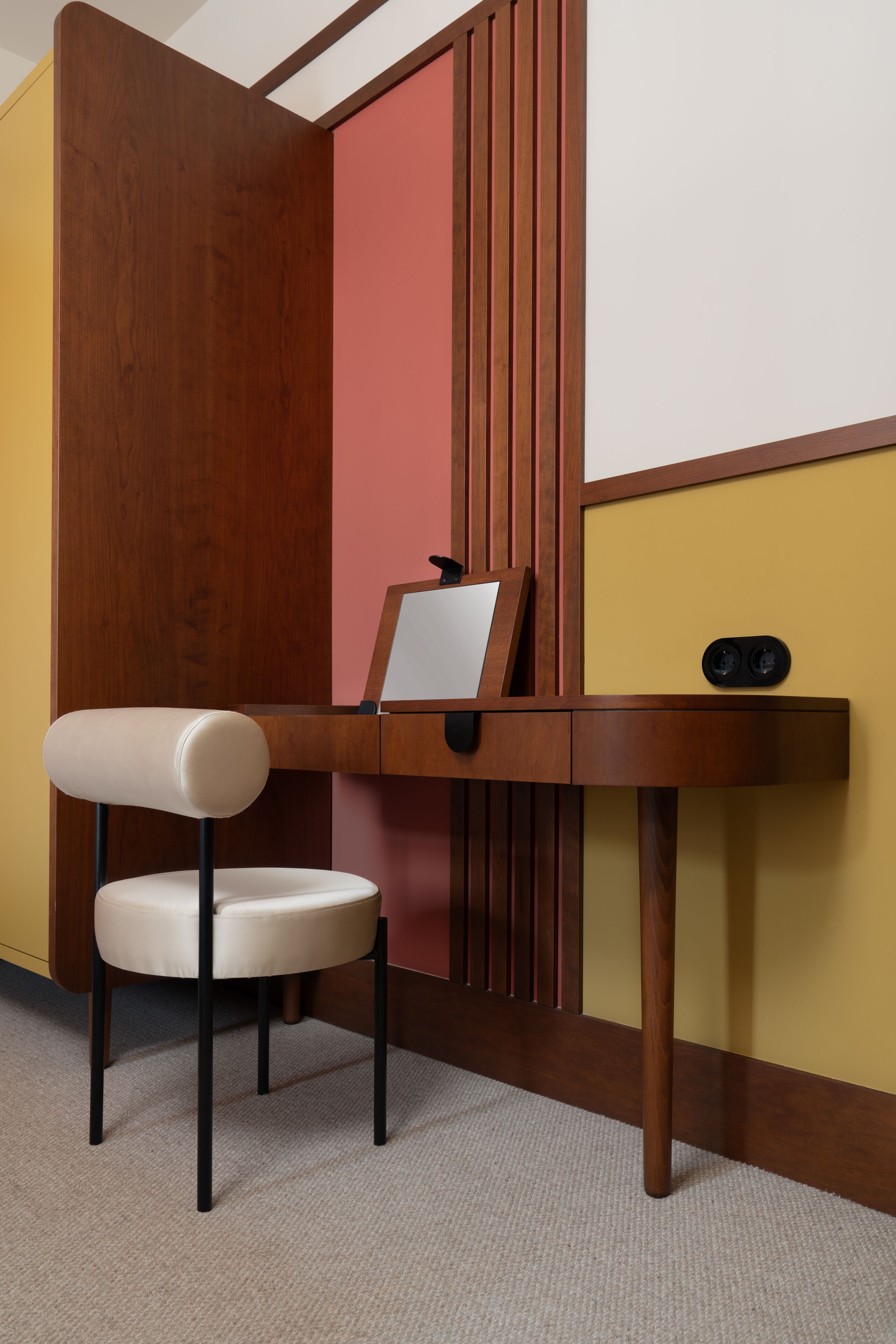 A wooden desk with a chair, a mirror, and a small black object on the desk.