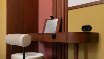 A wooden desk with a chair, a mirror, and a small black object on the desk.