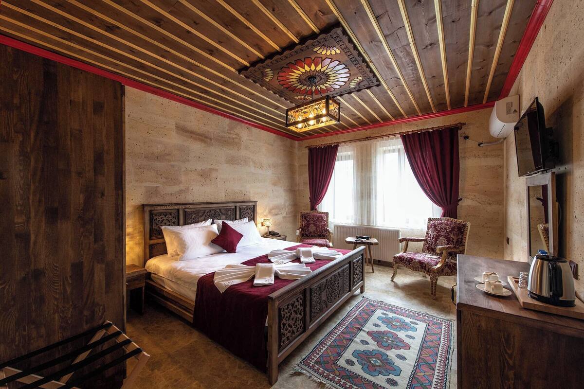 Quarto com cama de madeira, mesa de cabeceira, cadeira, escrivaninha e luminária decorativa no teto.