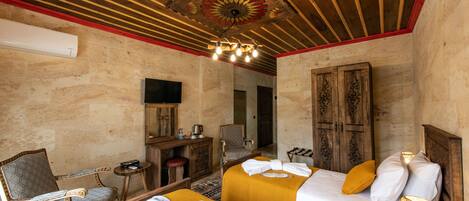 A hotel room with two beds, a wooden ceiling, a desk with a chair, and a television.