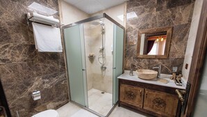 A bathroom with a glass-enclosed shower, a wooden vanity with a bowl sink, and a marble-tiled floor. - Volare Stone Hotel (Nevsehir)