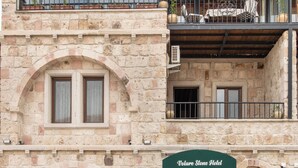 A stone building with a sign reading "Voltaire Stone Hotel". It features a balcony with a wooden ceiling and a chandelier, and a small outdoor seating area with tables and chairs. - Volare Stone Hotel (Nevsehir)