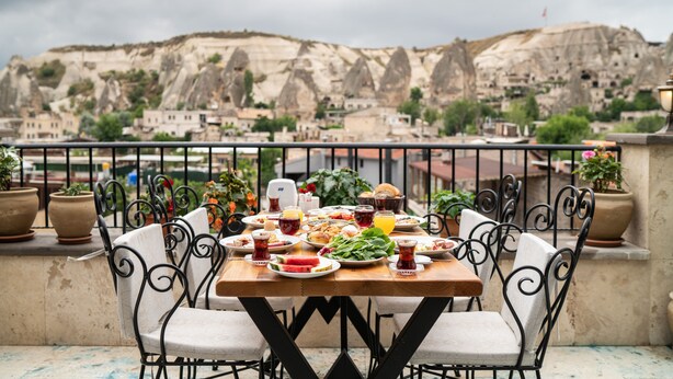 A table set with food and drinks on a balcony with a view of a mountainous landscape. - Volare Stone Hotel (Nevsehir)