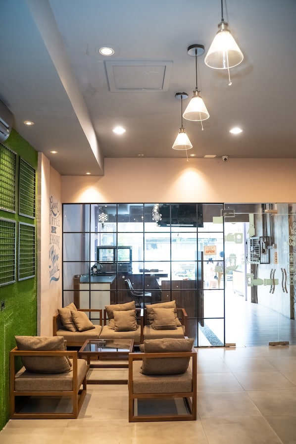 A modern interior with a seating area, a glass partition, and a visible coffee shop in the background. - Sahaja Pasar Baru (Jakarta)