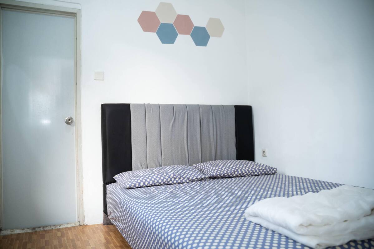 A bedroom with a bed, a grey headboard, a blue and white checkered bedspread, and a white blanket.