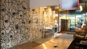 A modern interior with a glass wall, a flat-screen TV, and a wall with whimsical illustrations. - Sahaja Pasar Baru (Jakarta)