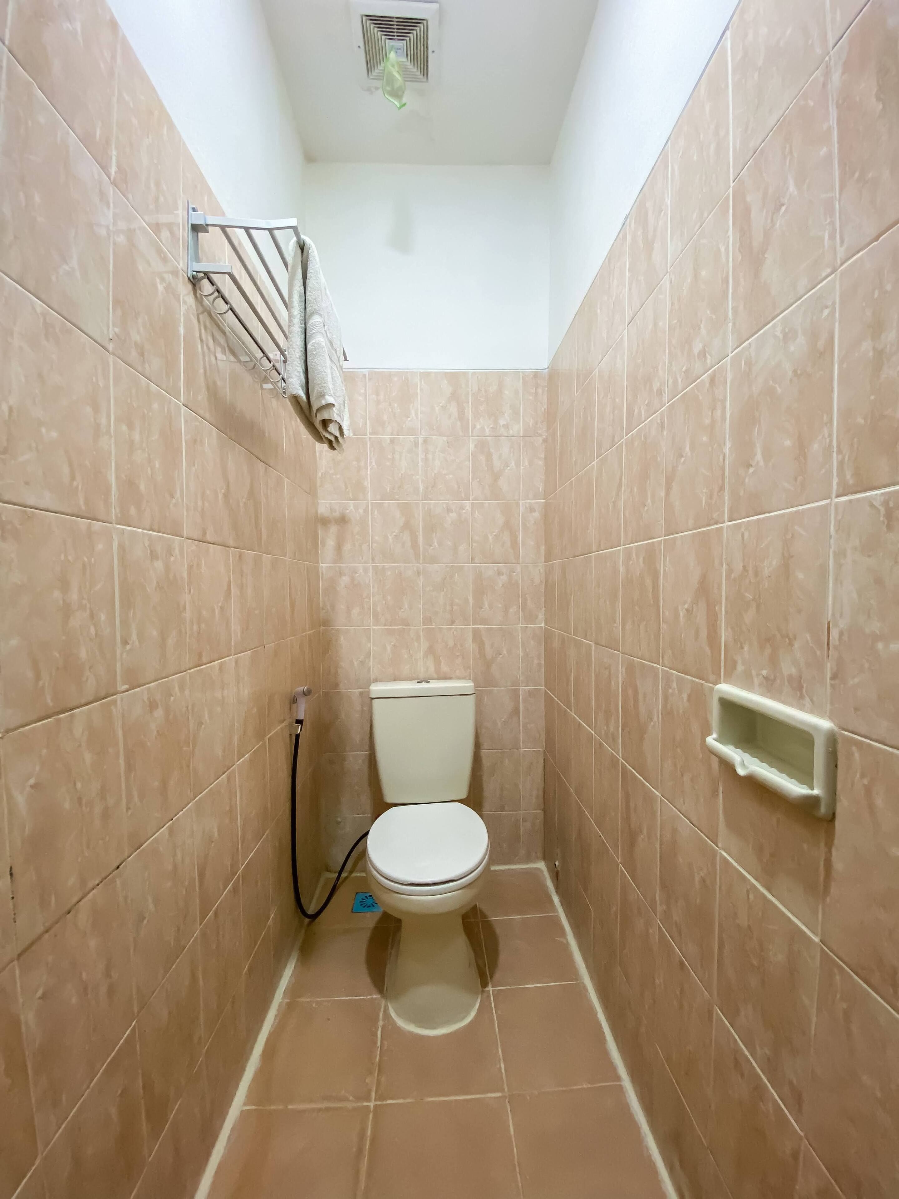 Une petite salle de bain avec des carreaux de couleur beige, des toilettes, un porte-serviettes et une grille d’aération au plafond.