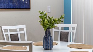 Una mesa de comedor con un jarrón azul y plantas verdes, rodeada de sillas blancas y individuales tejidas.