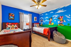 Een kamer met twee bedden, een plafondventilator en een muurschildering van tekenfilmfiguren.