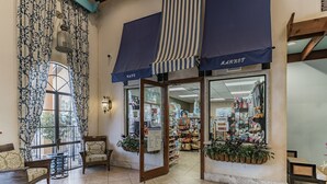 Una tienda con toldo azul, un amplio ventanal con cortinas estampadas y diversos artículos a la vista.