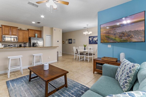 A modern kitchen with wooden cabinets, a refrigerator, and a dining area with a table and chairs. - Disney Getaway Oasis: 4BR Townhome, Heated Pool & BBQ, Perfect for Families! (Kissimmee)