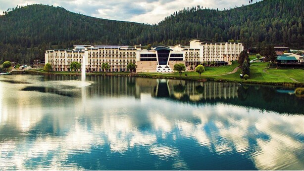 Un hotel con un ampio complesso di edifici affacciato su un lago, circondato da vegetazione e colline.