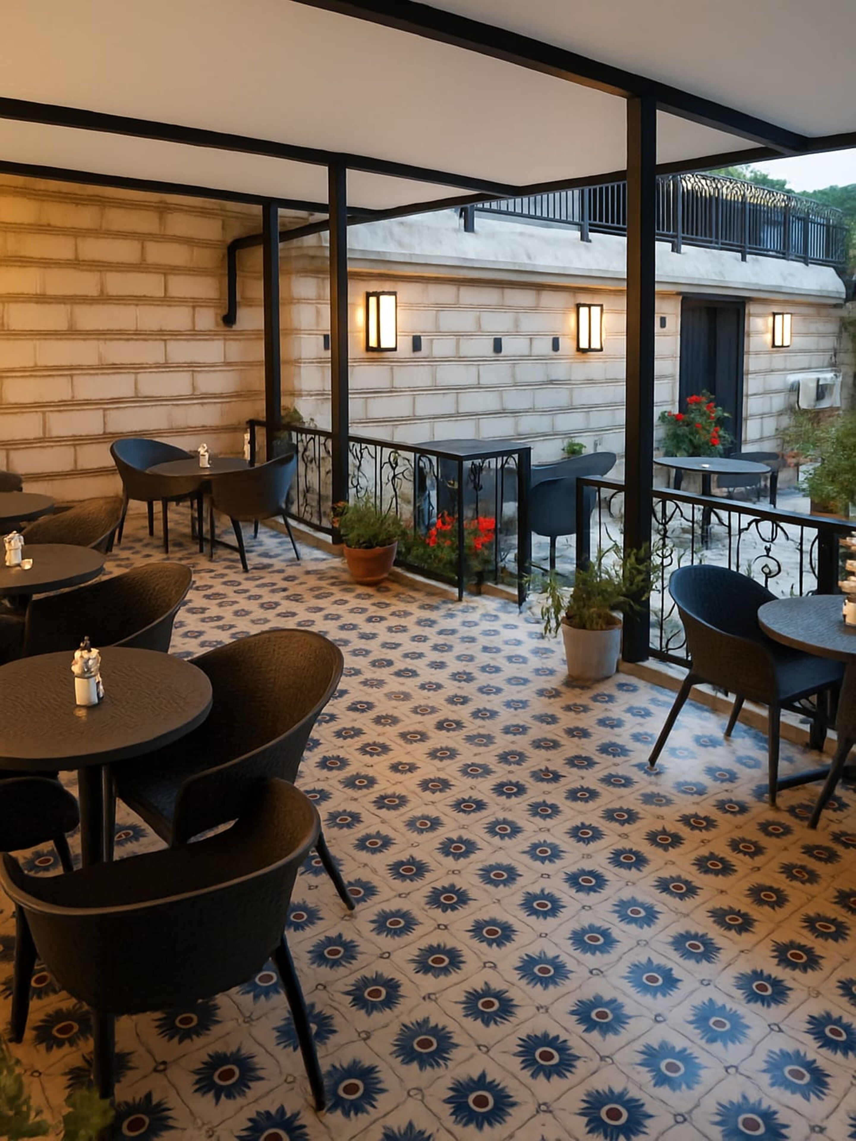 An outdoor patio with round tables and chairs, a patterned floor, and a view of a building with a balcony.