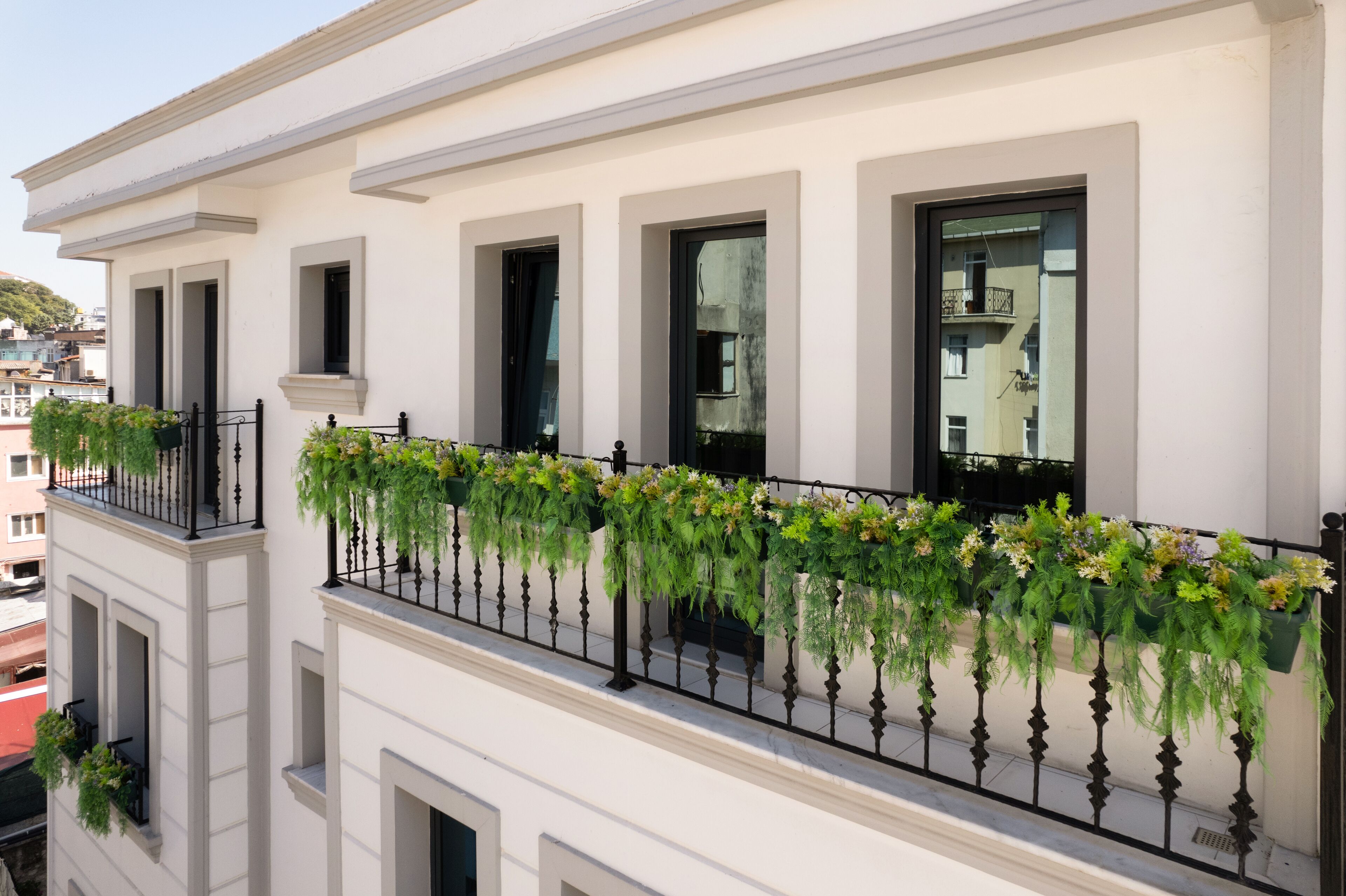 A white building with multiple balconies, each with black wrought iron railings and hanging flower boxes.