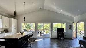 A spacious kitchen with a large island, a dining area with chairs, a TV, and a sliding glass door leading to an outdoor deck. - Spectacle Lake Waterfront Retreat Chalet (Tonasket)