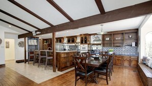 Een ruime keuken met houten kastjes, een eethoek met een grote tafel en stoelen, en een inbouwkookeiland met een spoelbak.