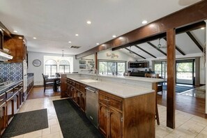 A spacious kitchen with wooden cabinets, a large island, and a view to the outdoors.