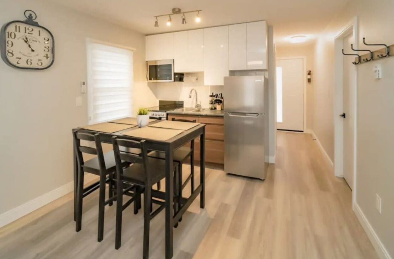 A modern kitchen with a dining table, chairs, a refrigerator, and a clock on the wall.