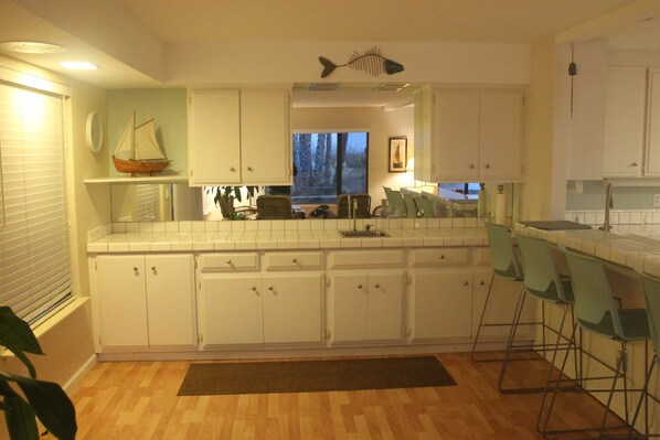 Une cuisine avec des meubles blancs, une décoration représentant un bateau en bois, une décoration murale en forme de poisson et une fenêtre donnant sur des arbres.