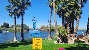 A serene lakeside view with a boat dock, palm trees, and a sign indicating a 5 MPH no wake zone.