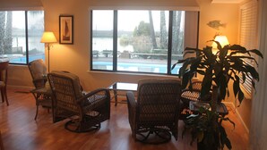 A room with wicker chairs, a table, a lamp, and a view of a lake.