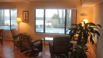 A room with wicker chairs, a table, a lamp, and a view of a lake.