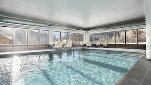 Ein Hallenbad mit klarem Wasser, großen Fenstern und Liegestühlen.