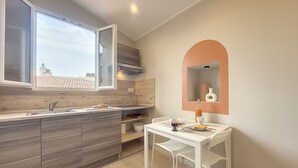 A modern kitchen with a large window, a dining area with a white table and chairs, and a small alcove with a mirror and decorative items. - N&J -  VIEUX NICE SUITE - Old Town - Close sea (Niza)
