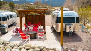 Ein Campingplatz mit Wohnmobilen, einem überdachten Picknickbereich mit roten Stühlen und einem felsigen Vordergrund.