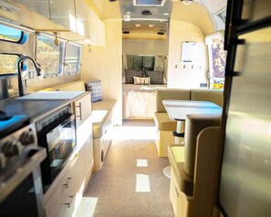Un intérieur de camping-car compact comprenant un coin cuisine, un espace repas et un espace nuit.