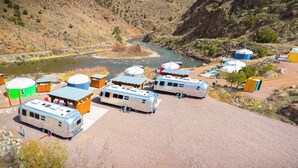 Um camping com veículos recreativos, iurtes e um rio.