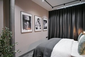 A modern bedroom with a large bed, a dark curtain, and three framed pictures on the wall. - Manhattan | The Heim Residences (Manchester)