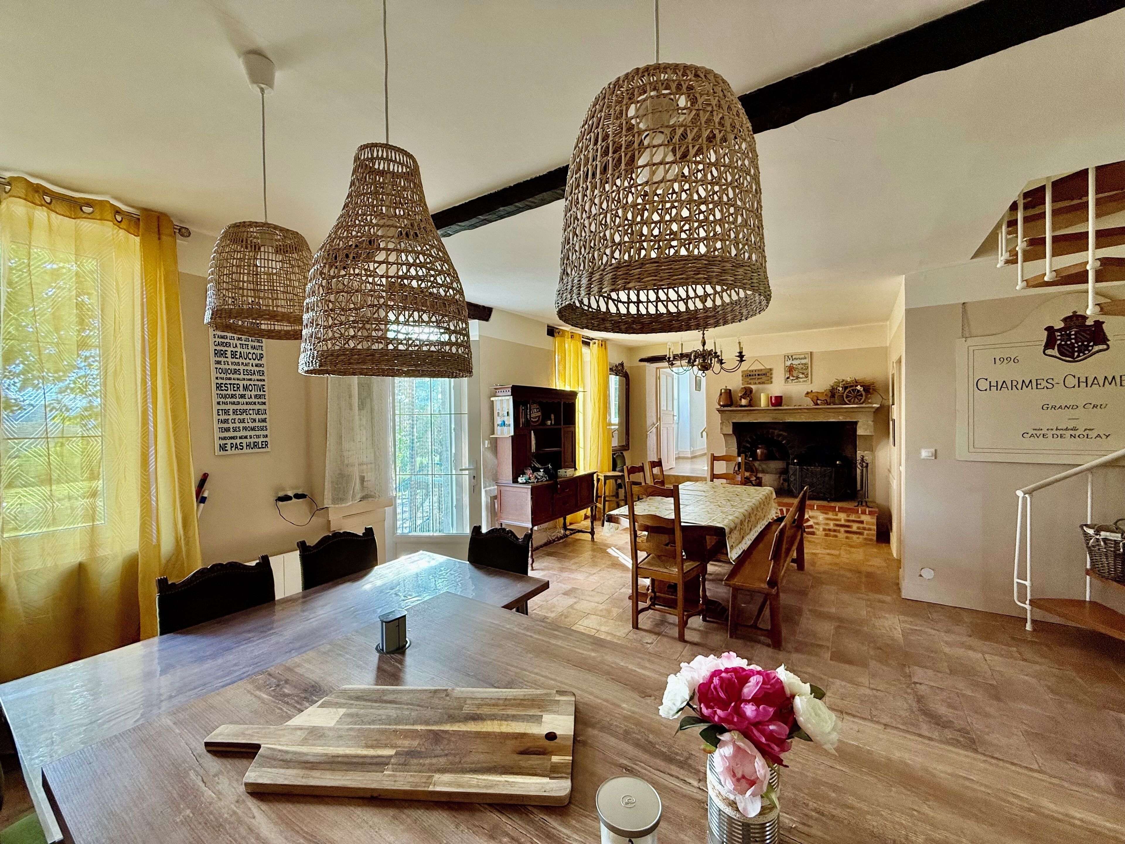 A dining area with a wooden table, wicker pendant lights, and a vase of flowers.
