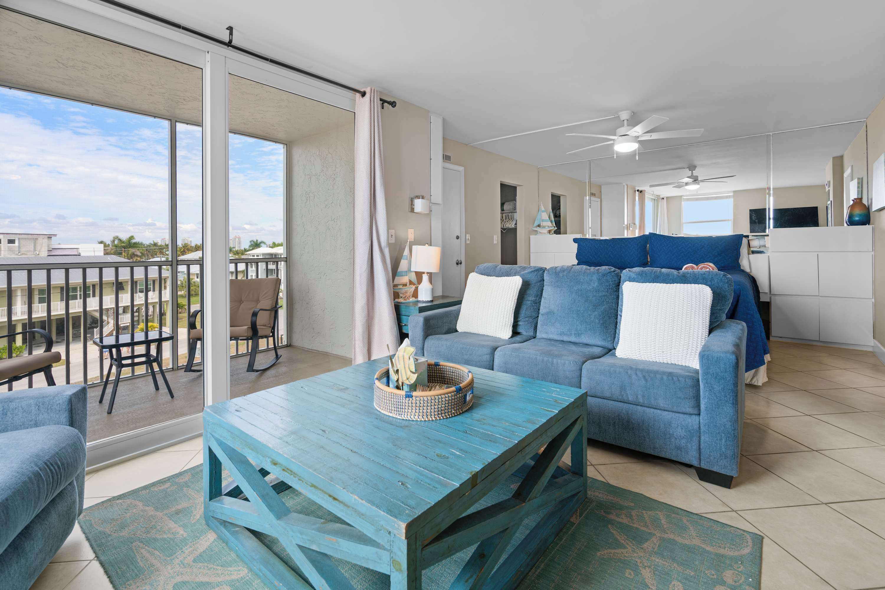 Een ruime woonkamer met een blauwe bank, een houten salontafel en een balkon met uitzicht op de stad.