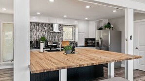 A modern kitchen with white cabinetry, a wooden island, and stainless steel appliances. - Amazing and Comfortable Home in Grand Prairie! (Grand Prairie)