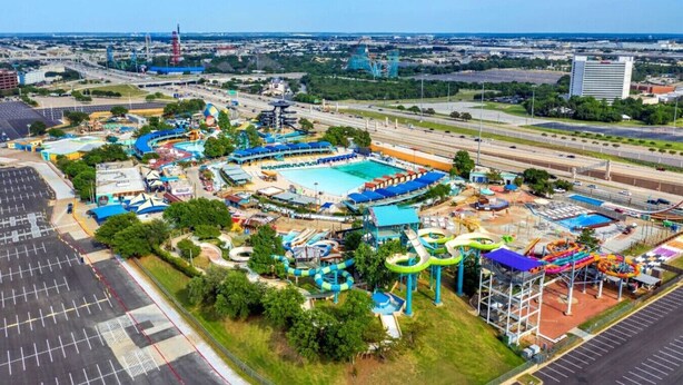 An aerial view of a theme park with a large swimming pool, water slides, and a parking lot. - Amazing and Comfortable Home in Grand Prairie! (Grand Prairie)
