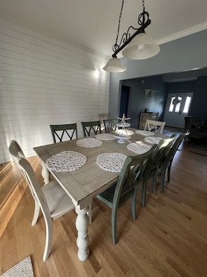 Uma sala de jantar com uma mesa de madeira, cadeiras brancas e um lustre.