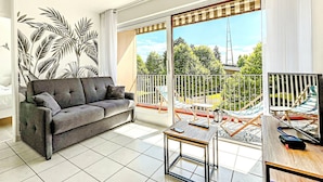 A living room with a grey sofa, a small table with a phone, and a balcony with outdoor furniture. - Annecy 1 bedroom Apt With Balcony (Annecy)